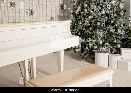 Close-up of silver and gold balls on the fir branch.Blurred old white piano and Christmas tree in the background. Stock Photo