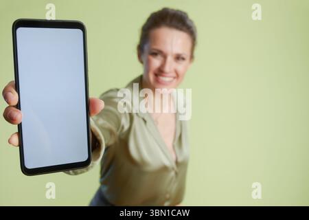 Smiling woman presenting a smartphone with a blank white screen. Engaging technology demonstration with a positive vibe. Stock Photo
