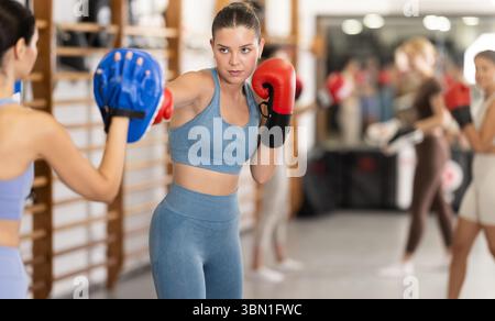 Woman works out strength and speed of boxing punch mitts with help of partner in boxing paws Stock Photo
