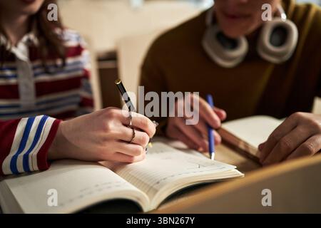 Caucasian young woman and Caucasian young man studying together at university, writing notes in notebooks, focusing on academic work, closeup of hands and books on desk Stock Photo