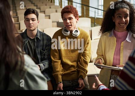 Group of multiethnic university students interacting in lecture hall, standing together in circle, discussing group assignment, talking while working on project Stock Photo