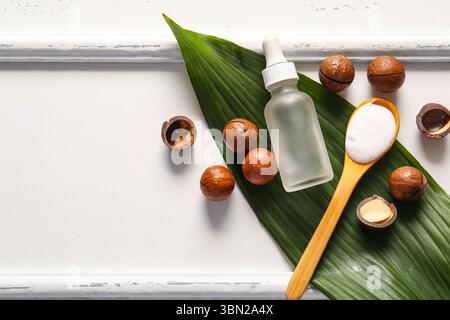 Macadamia nuts, green leaf, wooden spoon and bottle of cosmetic product on white background Stock Photo