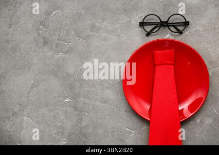 Plate with eyeglasses and origami tie from paper napkin on grey grunge background Stock Photo
