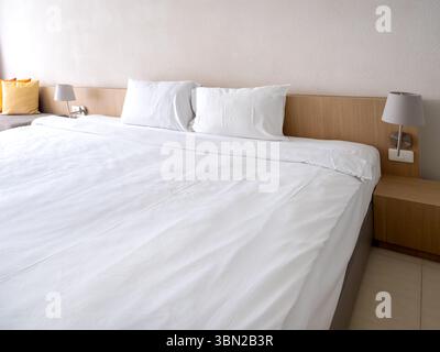 Scene of empty white clean bedroom in guest hotel room interior, white blanket with two pillows on simple wooden bed, near frosted glass partition and Stock Photo