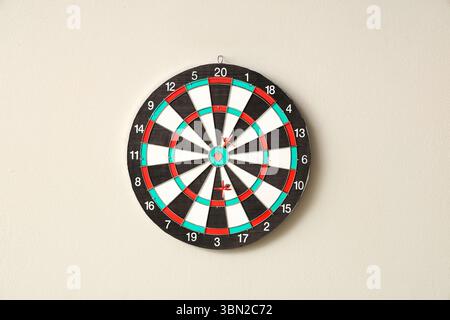 Board with darts hanging on light wall Stock Photo