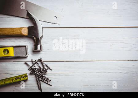Saw blade, hammer, level, nails and tape are being arranged on painted white plank, copy space Stock Photo