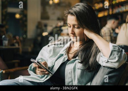 Hipster young woman reading text message on mobile phone at the cafe Stock Photo
