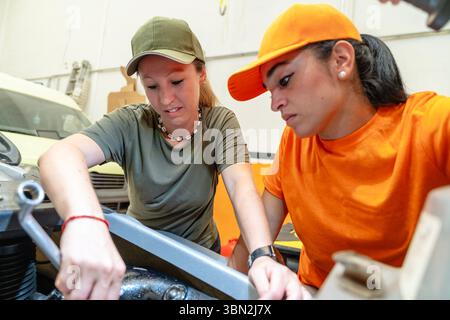 Two skilled female mechanics collaborate, using a wrench to fix a motorcycle engine in a professional garage Stock Photo