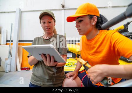 Two women mechanics are using a digital tablet and tools to repair a motorbike in a garage Stock Photo
