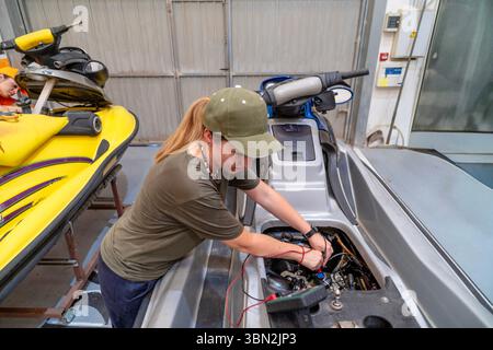 Female mechanic using multimeter checking engine of personal watercraft during maintenance in a jetski repair shop Stock Photo