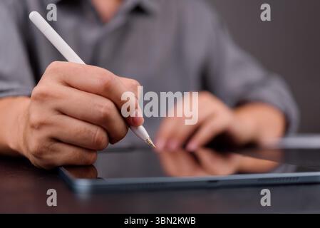 Close-up of hand using stylus on digital tablet, representing e-signature, paperless workflow, and modern business documentation. Stock Photo