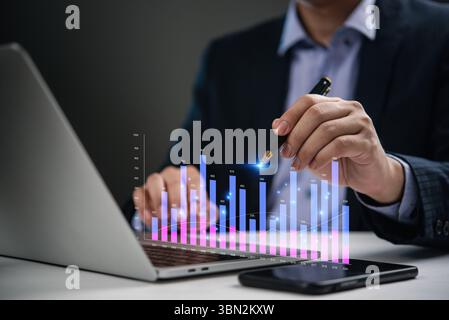 Businessman analyzing financial statistics on laptop with digital bar chart, business growth, economic trends, data analysis, and investment planning. Stock Photo