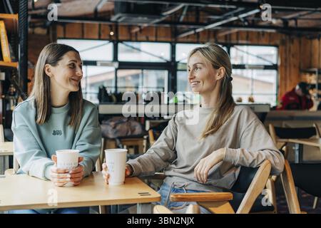 Two smiling happy female friends sitting in a coffee house, chatting and drinking coffee Stock Photo