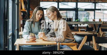 Two modern women make purchases on websites using a mobile phone Stock Photo