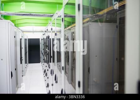 Server rack cabinets are lining aisle in flat design, featuring green beams and white floor tiles Stock Photo
