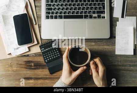 Top view of elegant female hands at workplace with laptop, calendar, coffee cup and bills Stock Photo