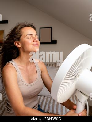 Woman feeling refreshed while cooling off with fan at home Stock Photo