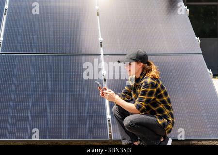 Female technician using smartphone to monitor solar panel performance remotely Stock Photo