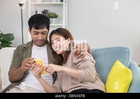 Happy asian young attractive couple use mobile phone online shopping. husband and wife happy with smart phone time together at home. Honeymoon , surfi Stock Photo