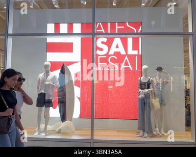 Woman Shopper Blends into Shop Window Featuring Sale Sign and Fashion Model Display in London Shopping Mall Stock Photo