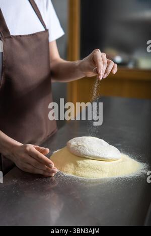 Close p of womans hands spreading flour on the dough while preparing pizza Stock Photo