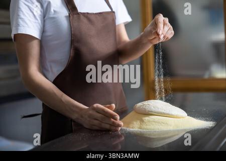 Close p of womans hands spreading flour on the dough while preparing pizza Stock Photo