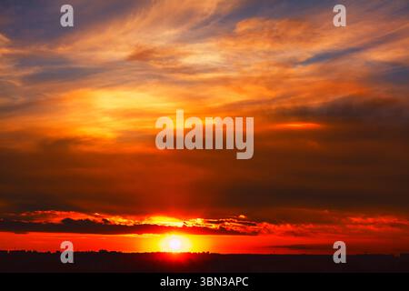 Dramatic sunset across the sky. Sun dips below the horizon, casting a fiery glow on the clouds. Twilight view with a rich palette of warm colors Stock Photo