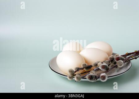 Plate with willow sprigs and white chicken eggs on a green background, copy space, selective focus Stock Photo