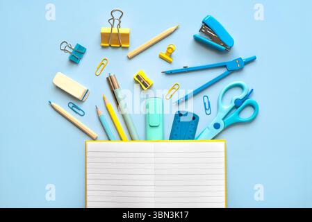 Top view of blank notepad open and school supplies with space for text over blue background. Back to school concept Stock Photo