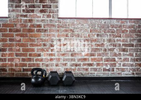 Kettlebell and hex dumbbells are resting on rubber mat against brick wall, flat design Stock Photo
