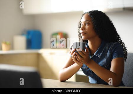 Black woman drinking and thinking alone in a kitchen at home Stock Photo