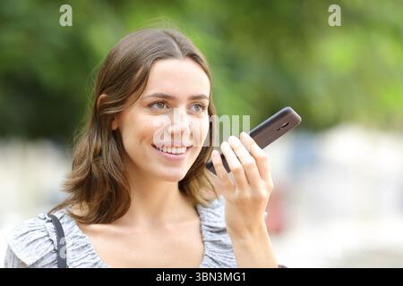 Happy woman dictating message on phone walking in the street Stock Photo