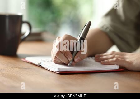 Close up portrait of a woman hand writing on paper agenda on wooden table at home Stock Photo