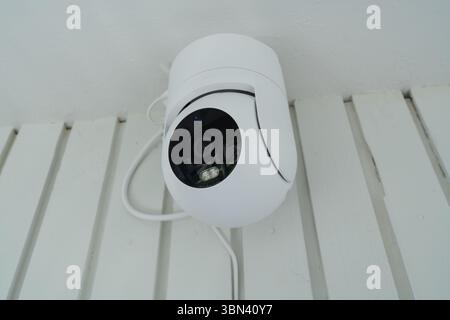 Modern white PTZ IP camera installed on a ceiling. Smart home technology concept for surveillance, safety, and security. Stock Photo
