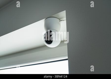 A modern PTZ IP camera of a smart home system. A white rotating surveillance camera installed on the ceiling for 24/7 monitoring. Stock Photo