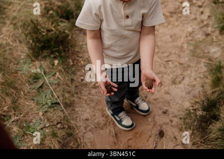 Child holding small pine cones on a dirt trail outdoors Stock Photo