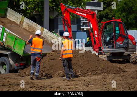 Two workers in fluorescent orange vests supervise the unloading of a truckload of topsoil. Stock Photo