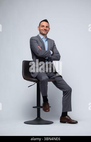 Professional Man in Gray Suit Sitting on Stool with Arms Crossed Stock Photo