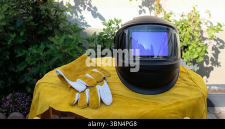 Industrial still life with welding helmet and bright leather protective clothing in a home interior. Gloves and an apron for a welder. Stock Photo