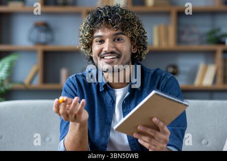 A smiling man with curly hair, dressed in a denim shirt, holding a notepad and pen, looking at the camera. Stock Photo
