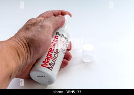 London. UK- 06.27.2025. A hand holding a bottle of Magnesium Muscle spray isolated on a white background. Stock Photo