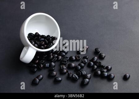 spilled black coffee beans from white cup on dark floor. Stock Photo