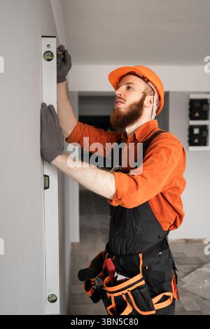 construction foreman using spirit level on concrete wall. Repairman wearing blue coveralls at construction site. Vertical video Stock Photo