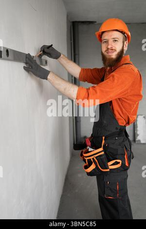 construction worker or engineer measures wall with a spirit level. Smiling to camera. Copy space Stock Photo