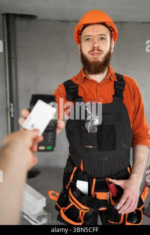 Builder holding a POS terminal during the client paying for the services of the builder and handyman with a credit card. Copy space Stock Photo