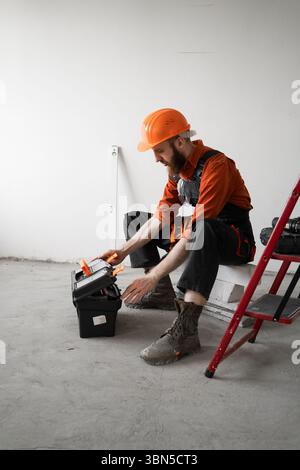 Repairman sitting near ladder opening toolbox before repairing at home or in office. Copy space Stock Photo
