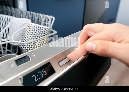 Man pushing start button on the control panel of the dishwasher. Stock Photo