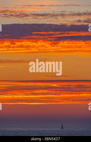 Lonely sailboat sailing under a breathtaking fiery sunset over the ocean Stock Photo