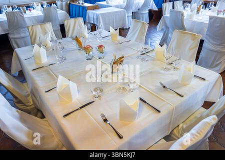 Empty restaurant tables are set with white tablecloths and silverware, ready for a formal event in Kitzeck im Sausal, Austria Stock Photo