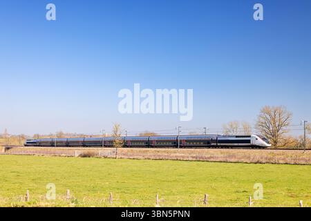 French tgv high speed train traveling through the green fields of the Bourgogne Franche Comte region, near Cortevaix, in Saone et Loire, France, under Stock Photo
